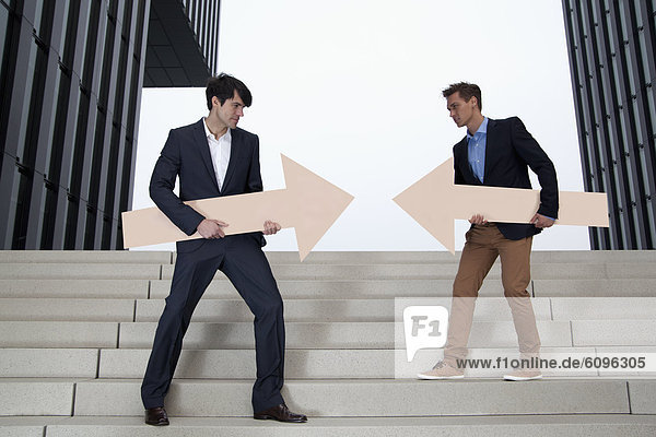 Germany  North Rhine Westphalia  Duesseldorf  Young businessmen standing on steps with arrows in different direction