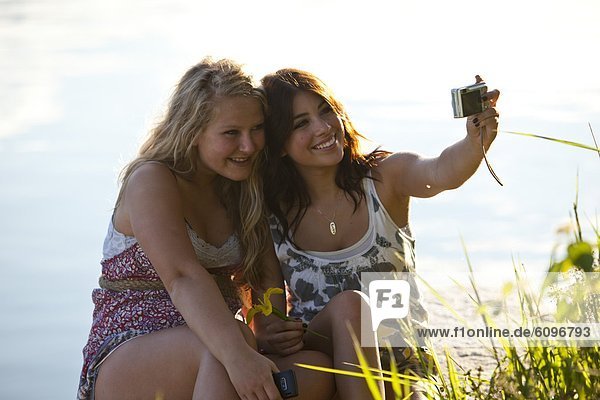 Two young women smile while taking a picture of themselves on a sunny day at the lake.