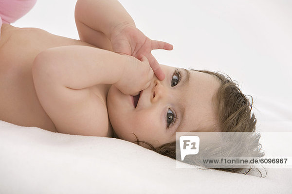 Baby girl lying on back with finger in mouth  smiling
