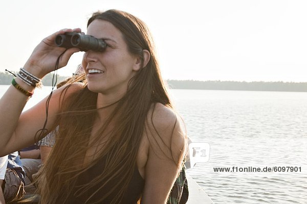 A young woman looks through binoculars at various types of birds on lake Sandoval in the amazon rainforest.