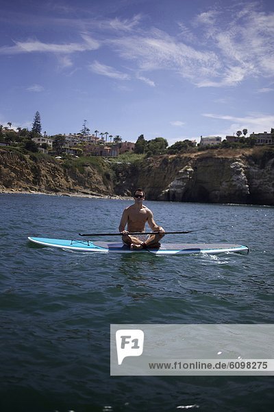 A male sits on his stand up paddle board.