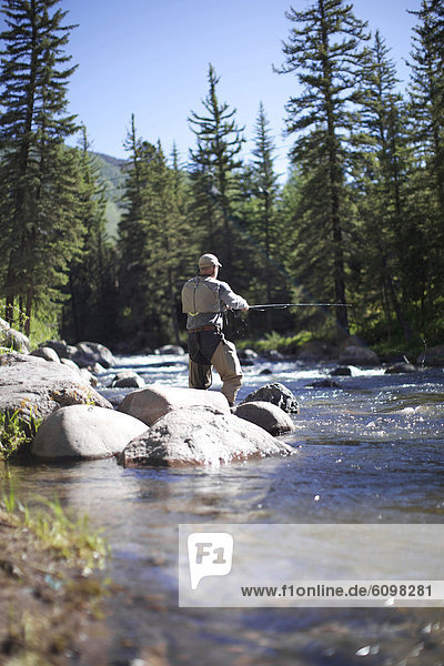 Fisherman standing by the rocks goes fly fishing at a river in Vail.