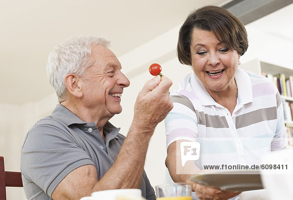 Senior man holding tomato and looking at woman