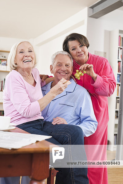 Seniorenfrauen füttern den Mann mit Trauben und Käse