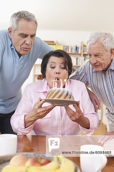 Ältere Männer und Frauen  die Kerzen auf Kuchen ausblasen.