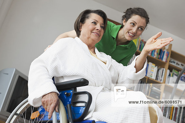 Senior woman sitting on wheelchair while another woman pushing