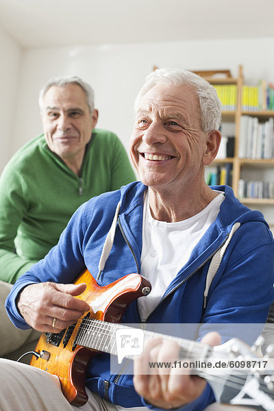 Senior Mann spielt E-Gitarre  Mann sitzt im Hintergrund