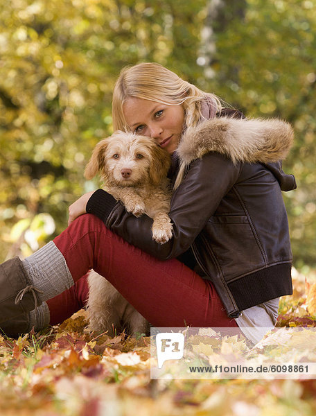 Österreich  Junge Frau sitzend mit Hund auf Herbstblatt  lächelnd  Portrait