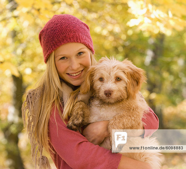 Österreich  Teenagermädchen hält Hund im Herbst  lächelnd  Portrait
