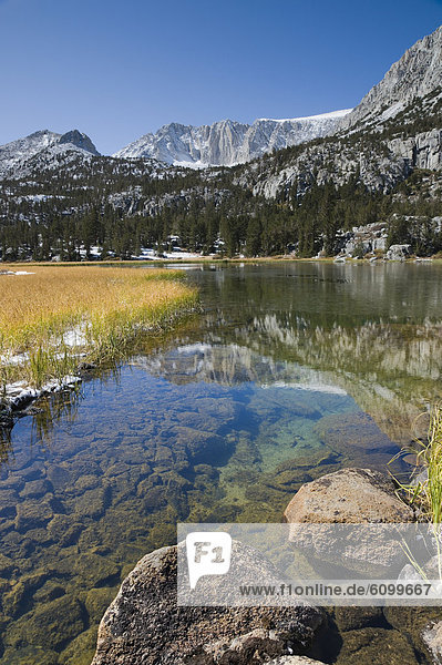 The High Sierra mountains with new fall snow reflecting in an alpine lake in Rock Creek Canyon in California