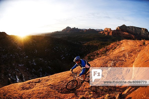 A middle age man rides his mountain bike through the red rock country around Sedona  Az at sunset.