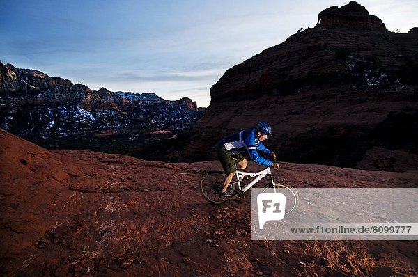 A middle age man rides his mountain bike through the red rock country around Sedona  Az at sunset.