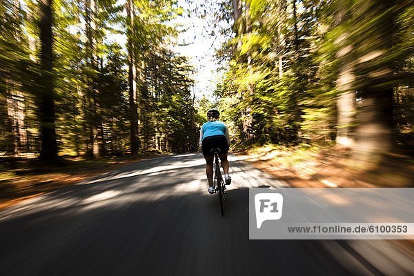 A female cyclist quickly rides on a small narrow road near Franconia  New Hampshire. Motion Blur.