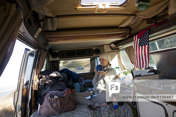 A young woman takes her morning coffee inside a Volkswagen Wesfalia camper van on the Pacific coast in southern Oregon