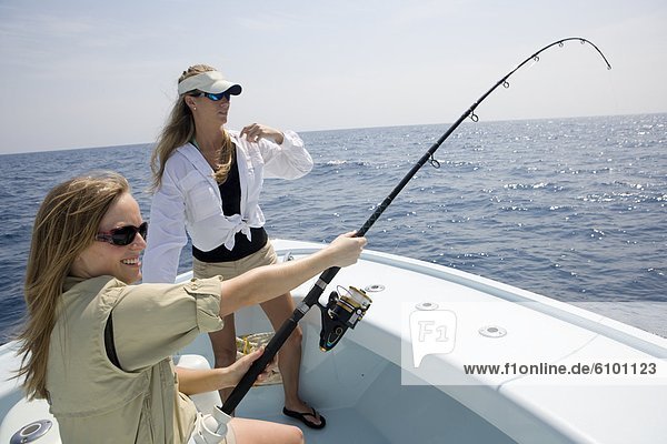 Two women are fishing on the bow of a boat with the rod bending on a catch.