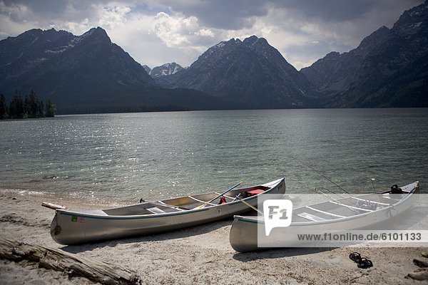 Two canoes are beached on the shore of Lake Leigh with the Grand Tetons in the distance.
