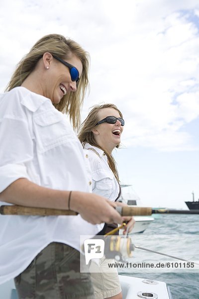 Two women are laughing while fishing off the side of a boat.