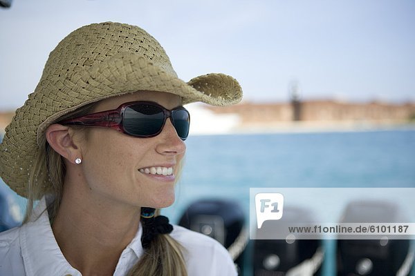A close-up of a blonde woman as she looks out to the water wearing sunglasses and a straw hat.