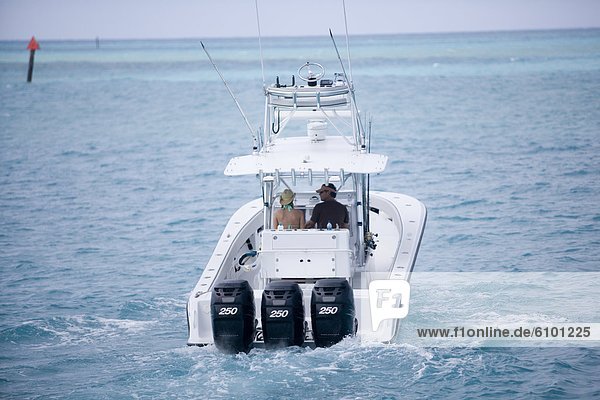 A man and woman on a fishing boat head out to blue-green water for a day of deep sea fishing.