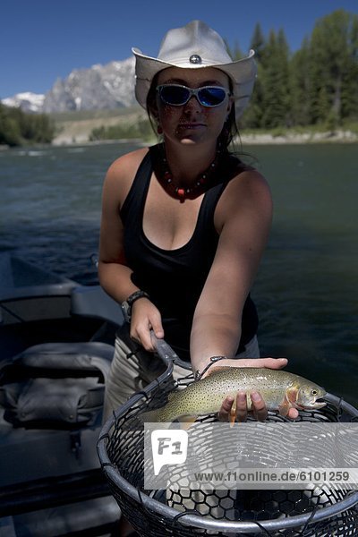 a young woman in a cowboy hat holding a fish net shows a cutthroat trout.