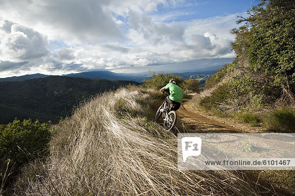 A young man rides his downhill mountain bike on Knapps Castle Trail  surrounded by beautiful scenery in Santa Barbara  CA.