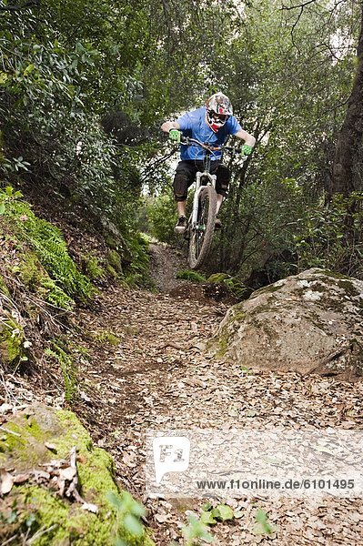 A young man rides his downhill mountain bike on Knapps Castle Trail  surrounded by beautiful scenery in Santa Barbara  CA.