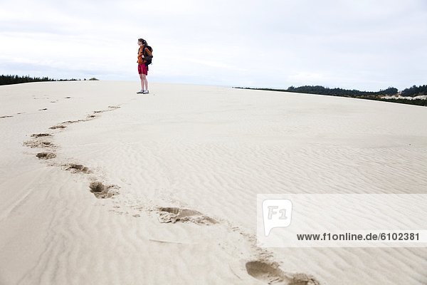 A girl walks alone on the sand dunes wearing a backpack.