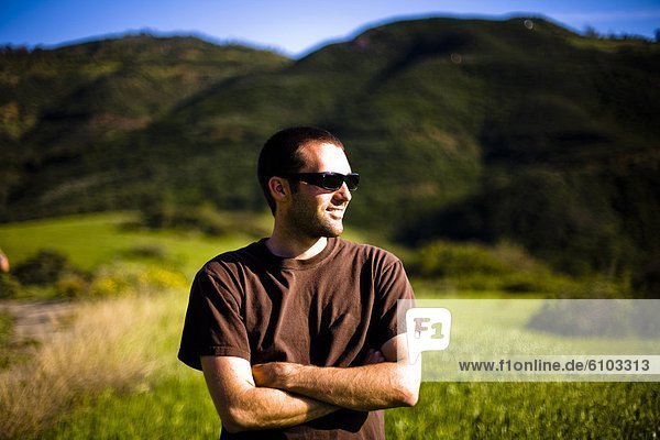 A male hiker wearing sunglass stops and looks at a field in the Santa Monica Mountains in Malibu  California.