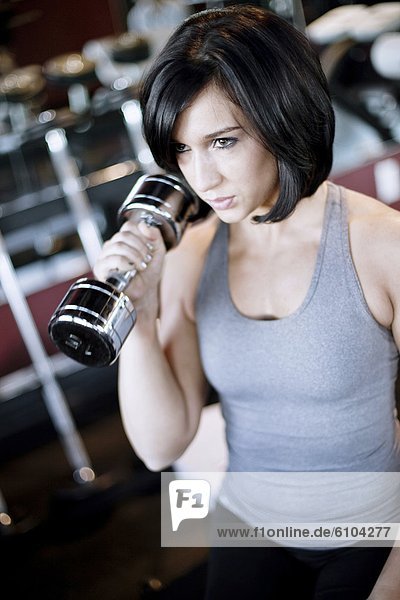 A young woman works out with free weights in a fitness gym.