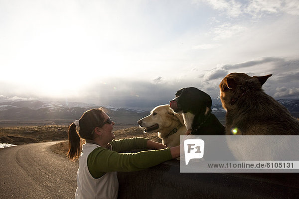 A woman smiles while petting here three dogs at sunset in Montana.