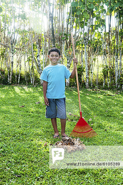 Boy standing next to a pile of raked leaves  Cook Islands.