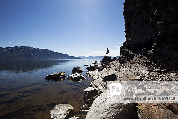 A male figure stands on a rock at the edge of a beautiful lake on a sunny day in Idaho.
