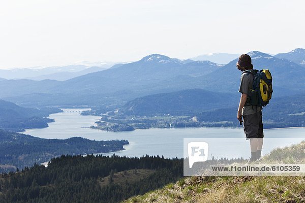 A young man backpacking looks out over a large river and Sandpoint  Idaho.
