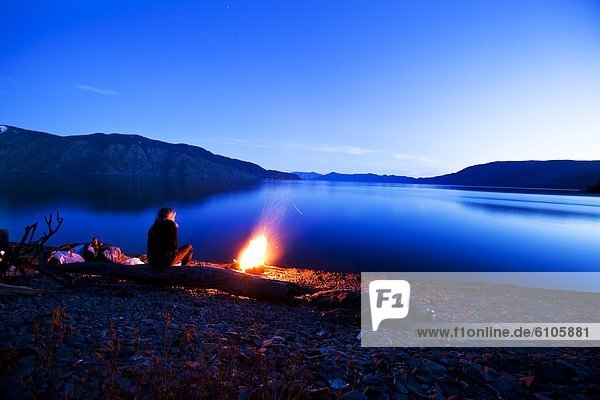 A woman sits next to a beautiful campfire at sunset in Idaho.