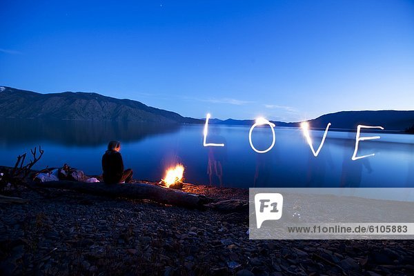 A woman sits next to a beautiful campfire at sunset with the word love next to her in Idaho.