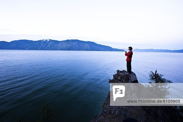 A handsome man peacefully stands on the edge of a cliff watching the sun rise over the lake in Idaho.
