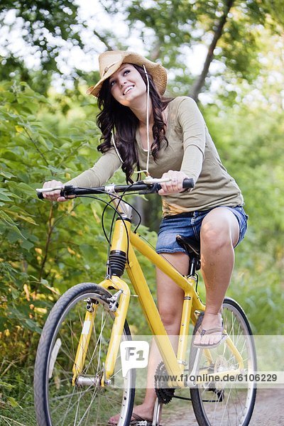 A smiling young woman rides a yellow bike down a dirt road.