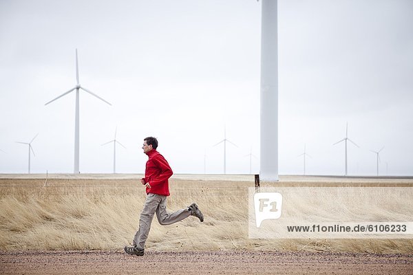 A man runs down a dirt road with windmills in the background  in the Pawnee Grasslands  Colorado.