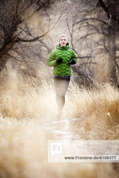 a young woman runs a down trail through dead grass just north of Dixon Reservoir  on a cold day in a green down jacket.
