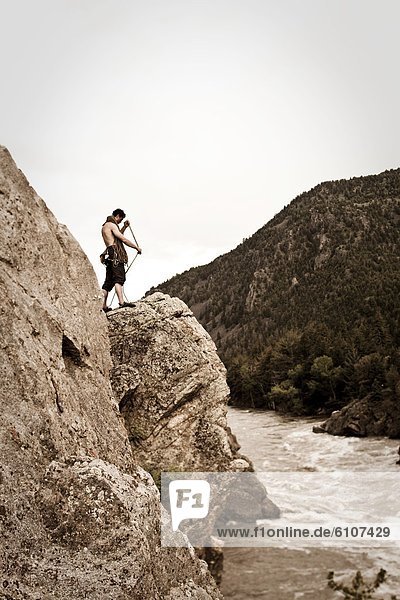 A athletic man coils a rock climbing rope next to a river in Montana.