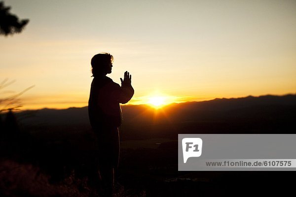 A young man praying as the sun rises over a valley in Idaho.