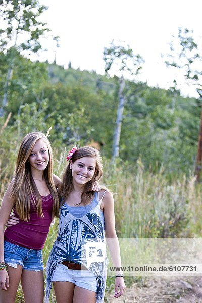 Two teen-aged girls smile at the camera - pictured along a country road.