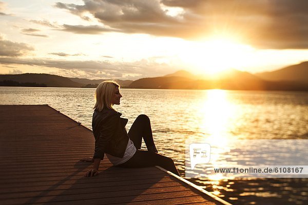A beautiful young woman sitting on a dock watching the sunset over a lake in Idaho.