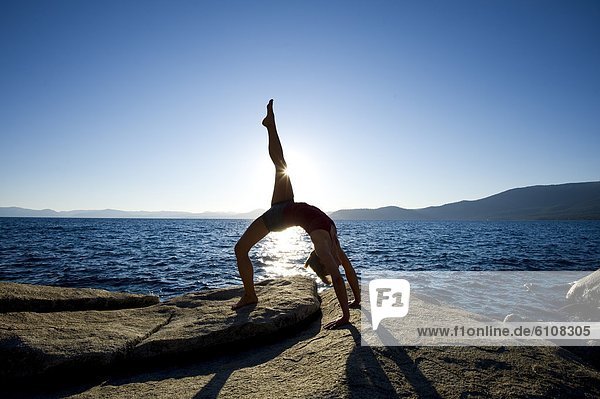 A silhouette of a young woman performing yoga on a granite boulder on the east shore of Lake Tahoe  NV.