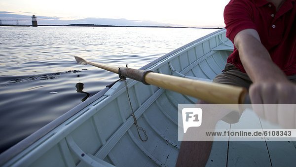 A young man rows in a Peapod dinghy at sunset along the coast of Maine near Boothbay Harbor.