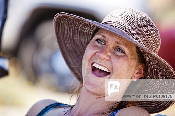 A woman laughs while wearing a sunhat on the shore of Bear Lake.