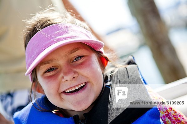 A five year old girl smiles while wearing a pink visor and a life jacket  Bear Lake  Utah.
