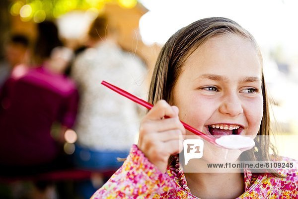 An eight year old girl  eats ice cream while sitting at red picnic table  Garden City  Utah.