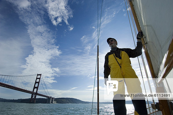A man holds onto the mast of his yacht while sailing.