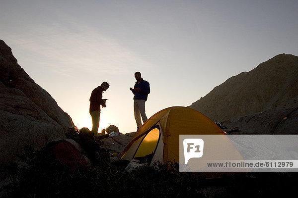Two men stand outside tent.